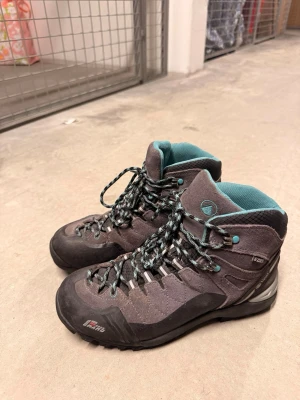 Grå turkosa kängor från Lippi - Säljer ett par grå kängor från Lippi med turkosa detaljer och snörning. Skorna har robust sula, vadderad insida och är tillverkade i mocka och syntet. Perfekta för utomhusaktiviteter och äventyr. Storlek 39.