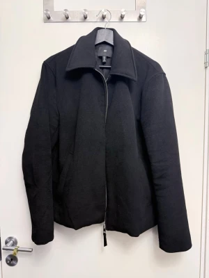 Svart ulljacka från H&M - Svart jacka från H&M i ullmix med klassisk krage och rak passform. Jackan har dragkedja framtill och två sidofickor. 