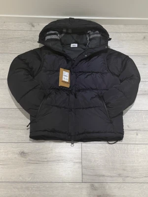 Svart pufferjacka från Burberry - Burberry jacka i storlek M, passar även S. Endast använd ett fåtal gånger och i mycket fint skick.  Pris: 2200kr Priset kan diskuteras vid snabb och smidig affär.