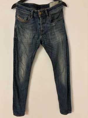 Blå skinny jeans från Diesel - Säljer ett par blå skinny jeans från Diesel med klassisk femficksdesign och snygga slitningar på benen. Jeansen har gul kontrastsöm och svart Diesel-märke bak i midjan. Perfekt passform för dig som gillar smalare siluett.