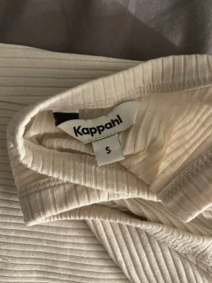 Ribbad vit långklänning Kappahl S - Säljer en ribbad långklänning från Kappahl i storlek S. Klänningen är vit, ärmlös och har en rundad hals. Materialet är mjukt och stretchigt, perfekt för dig som gillar enkel och stilren design. Passformen är normal och klänningen har ett snyggt ribbat mönster.