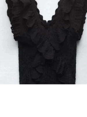 Svart spetsblus med volanger Zara  - Säljer en svart blus med djup v-ringning och stora volanger längs halsen och framtill. Blusen är gjord i spets med ett snyggt mönster och har korta ärmar. Perfekt för dig som gillar detaljer och vill sticka ut lite extra.