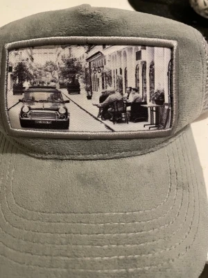 Grå mockakeps Emilio Pendenza - Snygg grå keps från Emilio Pendenza i mockaimitation med mesh på sidorna och ett svartvitt fototryck framtill. Kepsen har en cool urban vibe och justerbar baksida för perfekt passform.