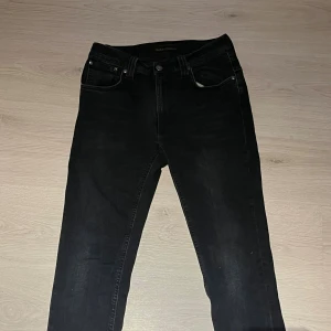 Mörk blåa jeans från Nudie Jeans - Mörk blåa jeans från Nudie Jeans med klassisk femficksdesign och snygga broderade detaljer på bakfickorna. Modellen har en rak passform och är tillverkad i mjukt jeanstyg som sitter skönt. Perfekt för dig som gillar stilrena och tidlösa jeans. Håll i högra fickan