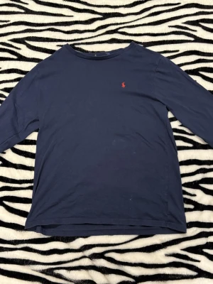 Ralph Lauren - Snygg mörkblå långärmad tröja från Polo Ralph Lauren med klassisk röd broderad logga på bröstet. Tröjan har 2 defekter, ena är lappen i nacken som gått av andra är det vi ser på sista bilden och det e nog lite smuts som går bort i tvätten. Storleken är XS. Hör av dig vid minsta fundering 😀 