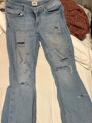 Ljusblå ripped jeans från 157 - Säljer ett par ljusblå jeans från 157 med flera slitningar och hål både fram och bak för en riktigt edgy look. Klassisk femficksmodell med raka ben och råa kanter vid fickorna. Perfekt för dig som gillar streetstyle och vill sticka ut.