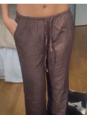 Bruna linnebyxor med snörning - Säljer ett par bruna linnebyxor med rak passform och snörning i midjan. Byxorna har sidofickor och är tillverkade i ett luftigt linnematerial som är perfekt för varmare dagar. Enkla att matcha med olika toppar och sneakers. Passar någon som kanske är typ 155 lång 