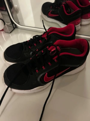 Svarta och röda Nike sneakers strl 42 - Nike sneakers i svart och rött med vit sula och röda detaljer. Skorna har mesh-överdel, snörning och en tydlig röd Nike-logga på sidan. Insidan är röd och sulan har mönstrade röda partier. Perfekt för träning.