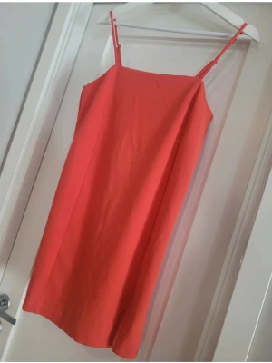 Röd kort klänning från Match - Snygg röd klänning med smala axelband och rak passform. Klänningen är kort och har en liten slits framtill för extra stil. Materialet känns mjukt och lätt, perfekt för varmare dagar. Enkel och stilren design som är lätt att matcha med accessoarer.