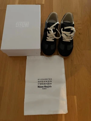 Maison Margiela marinblå sneakers ÄKTA - Maison Margiela sneakers i marinblå skinn och mocka med vita snören och beige innersida. Klassisk rund tå och platt gummisula i ljusbrun ton. Snygg minimalistisk design, levereras med originalkartong och dustbag. Passar 44