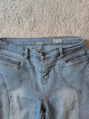 Blårandiga bootcut jeans från Authentic - Säljer ett par blå bootcut jeans från Authentic med smala vita ränder. Klassisk femficksmodell med knapp och dragkedja fram. Materialet är jeans och passformen är normal. Perfekt för dig som gillar retrovibbar och vill sticka ut lite extra.