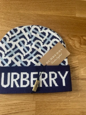 Blå och vit BB-mössa - Snygg mössa med blått och vitt mönster och stor logotyp framtill. Mössan har ett grafiskt, stickat mönster och bred uppvikt kant. Perfekt för dig som vill ha en trendig accessoar med lyxig känsla.