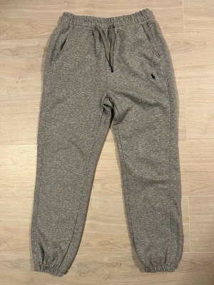 Grå mjukisbyxor från Polo Ralph Lauren - Säljer ett par grå mjukisbyxor från Polo Ralph Lauren med elastisk midja och snörning. Byxorna har sidofickor och den klassiska Polo-loggan broderad på vänster sida. Materialet är mjukt och skönt. Passformen är loose och muddar vid benslut. Även om de såklart passar på någon med storlek M tror jag att de hade passat bättre på någon med S och XS.