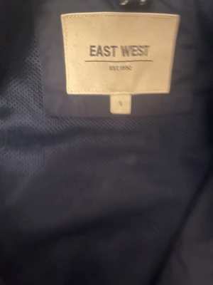 Svart jeansjacka från East West - Svart jeansjacka från East West med klassisk krage och dragkedja framtill. Jackan har två bröstfickor med knappar och två sidofickor. Perfekt för dig som gillar stilrena och tidlösa plagg.