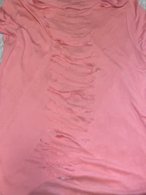 Rosa t-shirt med slitsad rygg - Cool rosa t-shirt med korta ärmar och unik slitsad design på ryggen. T-shirten är gjord i mjukt bomullsmaterial och har en loose passform. Perfekt för dig som vill sticka ut med en edgy och trendig look.