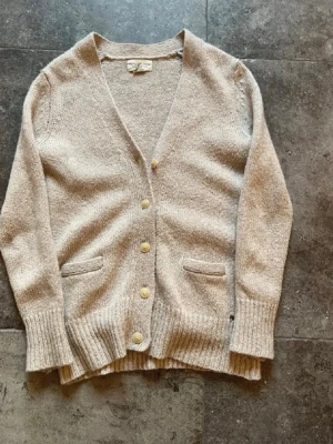 Beige kofta från Ralph Lauren - Säljer en beige stickad kofta från Ralph Lauren Denim & Supply. Koftan har v-ringning, ribbade muddar, fyra knappar framtill och två fickor. Perfekt för lager-på-lager och chill stil. Materialet är mjukt och skönt stickat.