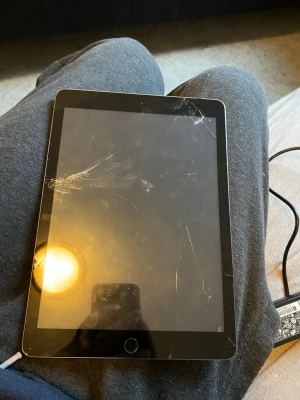 Apple iPad (med hemknapp) - Apple iPad med hemknapp. Skärmen har flera sprickor och repor, särskilt i övre vänstra hörnet. Perfekt för reservdelar eller reparation. Säljs i befintligt skick, laddare medföljer ej. och problem med batteriet