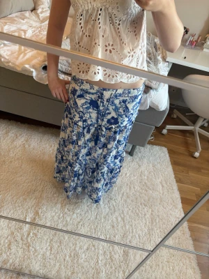 Blommig blåvit långkjol - Säljer en flowy långkjol med blått och vitt blommönster. Kjolen har volanger och en snygg snörning i midjan med tofsar. Perfekt inför sommaren till varma och mysiga sommarkvällar. Jag är 167 som referens. 🤍🤍