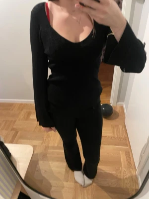 Svart ribbad stickad tröja AWARE - Svart stickad tröja från AWARE i storlek L. Tröjan har ribbad struktur, djup v-ringning och långa ärmar med lite utsvängda muddar. Snygg och enkel modell som är lätt att matcha med olika outfits.