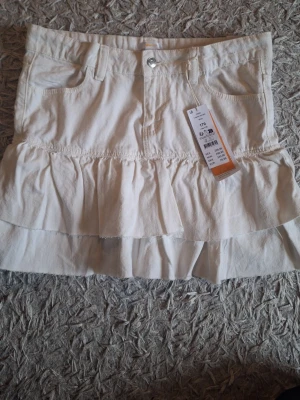 Vit volangkjol i denim  - Säljer en vit kortkjol i denim med volangdetaljer från Gina Tricot. Aldrig använd med prislappen på.