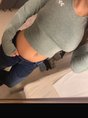 Grön croppad långärmad topp - Säljer en grön croppad långärmad topp  med rund hals och diskret logga på bröstet. Toppen är slim fit och tillverkad i ett mjukt syntetmaterial som passar perfekt till träning eller chill. Snygg och enkel att matcha med jeans eller tights.