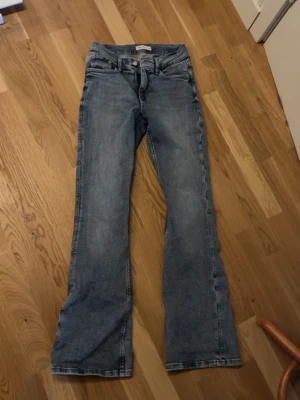 Blå bootcut jeans - Snygga blå jeans med klassisk bootcut-snitt och fem fickor. Jeansen har en lätt tvättad look och normal passform, perfekta för en chill och avslappnad stil. Materialet är jeans och midjan är midwaist. Passar dig som gillar retrovibbar och bekväma byxor. Aldrig använt 