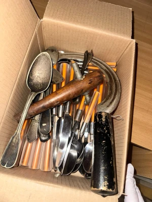 Bestick och verktyg Diverse Blandning av Bestick och Redskap - Bilderna visar en kartong med bestick och verktyg.Ett varierat sortiment av bestick och redskap. Inkluderar skedar, knivar, gafflar och andra diverse köksredskap.