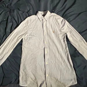 Ljusblå skjorta från Ralph Lauren - Klassisk ljusblå skjorta från Ralph Lauren med broderad logga på bröstet. Skjortan har lång ärm, knappar hela vägen och är tillverkad i mjuk bomull. Perfekt för dig som gillar stilren och tidlös design.