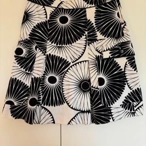 Svartvit midikjol från By Malene Birger, storlek 38 - Säljer en snygg midikjol från By Malene Birger med svartvitt grafiskt blommigt mönster och ficka med knapp framtill. Kjolen har ett foder med stora svarta prickar och är tillverkad i ett stadigt bomullstyg som ger bra form. Perfekt skick!