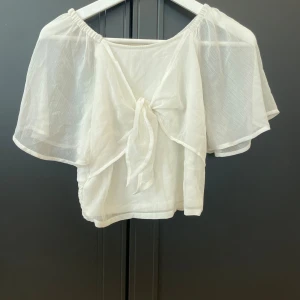 Vit blus med knyt från Lindex - Säljer en luftig vit blus från Lindex i storlek 158/164. Blusen har korta, vida ärmar och en snygg knytning framtill.