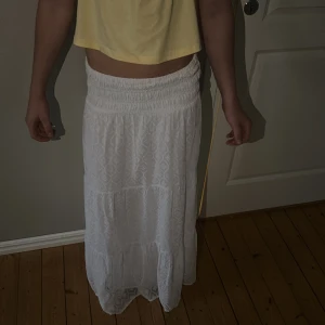 Vit långkjol med broderat mönster - Säljer en vit långkjol med broderat mönster och bred resår i midjan. Kjolen har en luftig och flowy känsla, perfekt för varma dagar. Tyget är lätt och har en snygg struktur med diskreta detaljer. Superfin att styla med crop top eller linne!