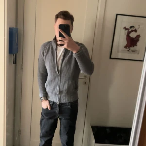 Grå stickad kofta från Blue Ridge - Säljer en grå stickad kofta från Blue Ridge i storlek S. Koftan har grovstickad struktur, hög ribbad krage och dragkedja framtill. Långärmad modell med två fickor och diskret logotyp på ärmen. Perfekt för lager-på-lager och chill stil. Priset kan diskuteras!!!