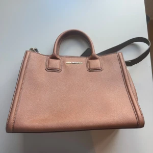 Brun handväska från Karl Lagerfeld - Snygg brun handväska från Karl Lagerfeld i stilren design. Väskan har två rejäla handtag, avtagbar axelrem i svart och guldfärgade metalldetaljer. Tillverkad i strukturerat skinn med diskret logga framtill. Perfekt för dig som vill ha en klassisk och trendig accessoar.