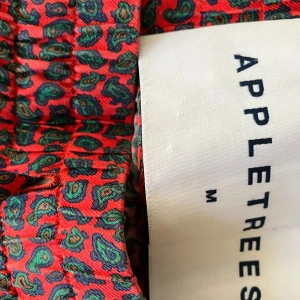 Weekend pant lake Como silk från Appletrees - Snygga röda sidenbyxor från Appletrees med paisleyinspirerat mönster i grönt och blått. Byxorna har resår i midjan för skön passform och är tillverkade i 100% siden som känns lyxigt. Perfekta för dig som vill sticka ut med färg och mönster. Nypris 7995 kr