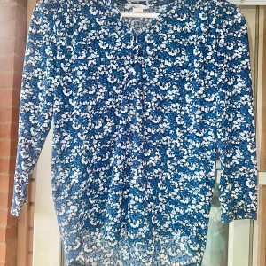 Blommig blus XS - Supersöt blå blus från H&M i storlek XS med vitt och mörkblått blommönster. Blusen har lång ärm, v-ringning och är gjord i mjuk polyester. Perfekt för dig som gillar färg och mönster!
