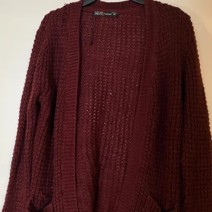 Vinröd stickad kofta Fast Fashion - Mysig vinröd stickad kofta från Fast Fashion i storlek  m Koftan har grovstickad struktur, långa ärmar och ribbade muddar samt kant. Perfekt att slänga på sig när det är kyligt ute.