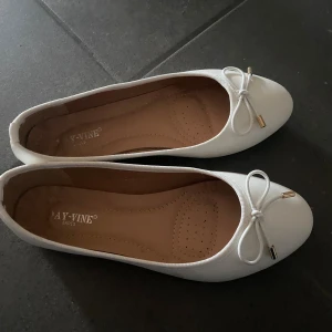 Vita ballerinaskor - Snygga vita ballerinaskor med rund tå och dekorativ rosett framtill. Skorna har en klassisk och stilren design med mjuk innersula och är jätte sköna. Perfekta att matcha till både jeans och klänning. Knappt använda