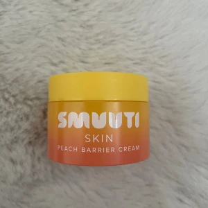 Smuuti Skin Peach Barrier Cream - Fuktgivande ansiktskräm från Smuuti Skin i en snygg burk med gul lock och persikofärgad botten. Perfekt för att stärka hudbarriären och ge huden en fräsch känsla. Innehåller persikoextrakt för extra glow. Säljer till någon som använder krämen dagligen. 