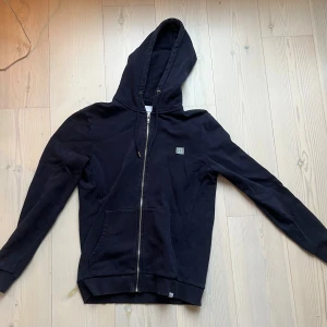 Mörkblå hoodie från Les Deux med dragkedja - Mörkblå hoodie från Les Deux med dragkedja framtill, huva med snörning och två fickor. Mjuk insida och diskret logga på bröstet. Perfekt för chill dagar eller när du vill ha en clean streetstyle-look.