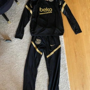 Nike träningsset svart guld - Nike FCB, oanvänt. Passar S/M. Skriv om ni vill ha fler bilder eller undrar vad som helst 🤗mått:  Byxor: midja= 30cm. Innerbenslängd= 73cm Tröja: bredd= 48cm innerarmslängd= 47cm längd på hela= 67cm  axelbredd= ca 52cm