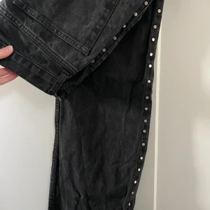 Svarta jeans med nitar från mango - Svarta jeans från mango med raka ben och silverfärgade detaljer längs sidorna. Jeansen har klassiska bakfickor och är tillverkade i ett robust denimtyg. Jag är 170 och de är långa på mig, midjan är mellan låg!