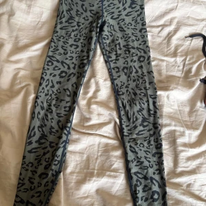 Leopardmönstrade leggings i grått - Snygga leggings med leopardmönster i grå och svart ton. De är tighta och har en bekväm passform, perfekta för dig som vill sticka ut lite extra. Materialet känns mjukt och följsamt mot huden. Perfekt till träning!