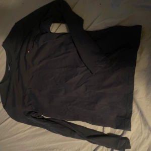 Svart långärmad tröja Tommy Hilfiger - Svart långärmad tröja från Tommy Hilfiger i mjuk ekologisk bomull. Klassisk rund halsringning och diskret logga på bröstet. Perfekt basic-plagg med stilren look som funkar till allt.