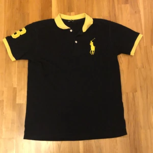 Svart och gul pikétröja Polo Ralph Lauren - Svart pikétröja från Polo Ralph Lauren i storlek XXL men sitter som M-S med gula detaljer på krage, ärmslut och stor gul logga på bröstet. Snygg gul siffra 3 på ena ärmen. 