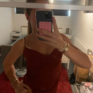 Vinröd linnetopp med spetsdetalj - Säljer en vinröd linnetopp med tunna axelband. Toppen har en lätt draperad framsida och är figurnära. Perfekt att styla med kjol eller jeans för en snygg look.