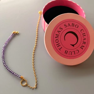 Lila pärlarmband från Thomas Sabo - Stilrent armband från Thomas Sabo Charm Club med lila facetterade pärlor och guldfärgad kedja. Armbandet har en rund berlock med logga och smidig karbinhake. Perfekt accessoar för att lyfta din look med lite färg och elegans. Äkta ametist på.