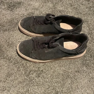 Svarta sneakers från Gant i mocka - Snygga svarta sneakers från Gant i mocka med svarta skosnören och detaljer i svart skinn vid hälen. Yttersulan är beige med röd undersida. Klassisk och stilren design med rund tå och platt sula. Perfekta för dig som gillar en clean look. Storlek 41 men skulle säga att den sitter som 41 1/2