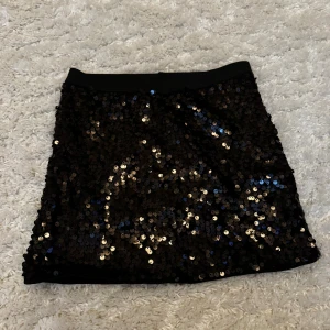 Svart paljettkjol från Lindex Kids - Glittrig svart kortkjol från Lindex Kids, täckt med svarta paljetter som reflekterar ljuset snyggt. Kjolen har en rak passform och elastisk midja för extra komfort. Perfekt för dig som vill sticka ut med en cool och festlig look.                                    (Storlek - 134/140)                                                     Skickar ditt köp inom 24h!💘                            