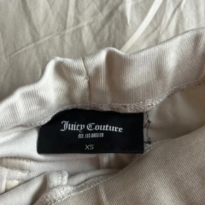 Vita mjukisbyxor Juicy Couture XS - Vita mjukisbyxor från Juicy Couture i storlek XS. Byxorna har snörning i midjan, raka ben och bakfickor med knappdetalj. Bakdelen av ena knappen fattas! Tillverkade i mjukt frottématerial som ger en chill och lyxig känsla.