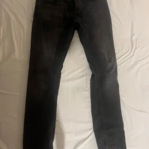 Svarta jeans från Nudie Jeans Co - Säljer ett par svarta grim tim jeans från Nudie Jeans Co med klassisk femficksdesign och silverfärgade nitar. Jeansen har en rak passform och är tillverkade i slitstarkt denimtyg. Perfekta för dig som gillar en stilren och enkel look. Pris kan diskuteras.